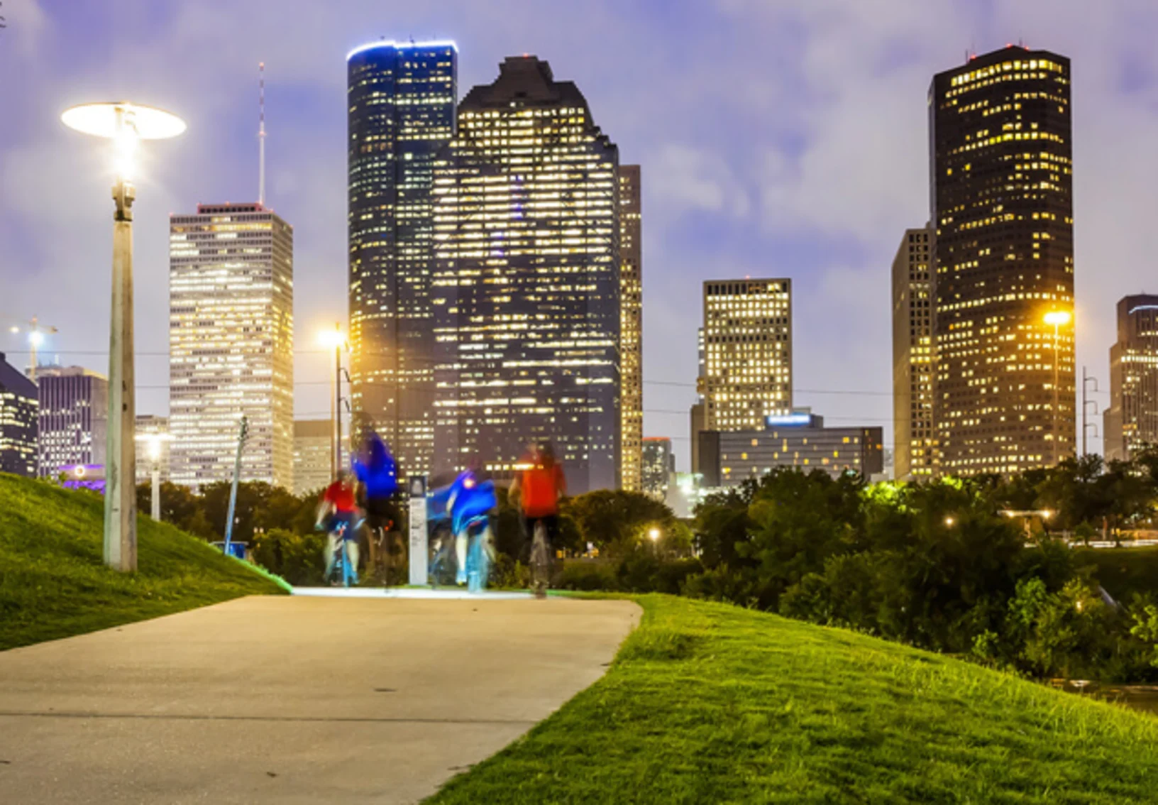 people walk through a park with the Houston, TX skyline in the background